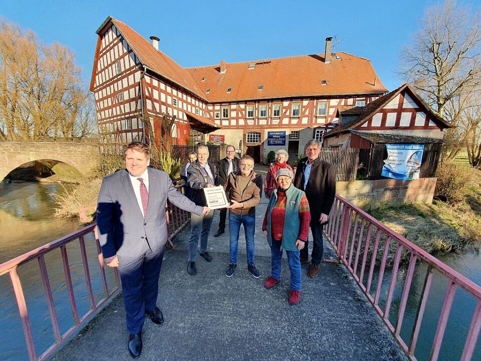 Der Erste Kreisbeigeordnete Marian Zachow (li.) über gaben im Beisein von Amöneburgs Bürgermeister Michael Plettenberg (re.) sowie Vertreterinnen und Vertretern des Brücker Vereins die offizielle Hinweistafel an Müllermeister Thomas Kleinschmidt. (Foto: Landkreis Marburg-Biedenkopf)